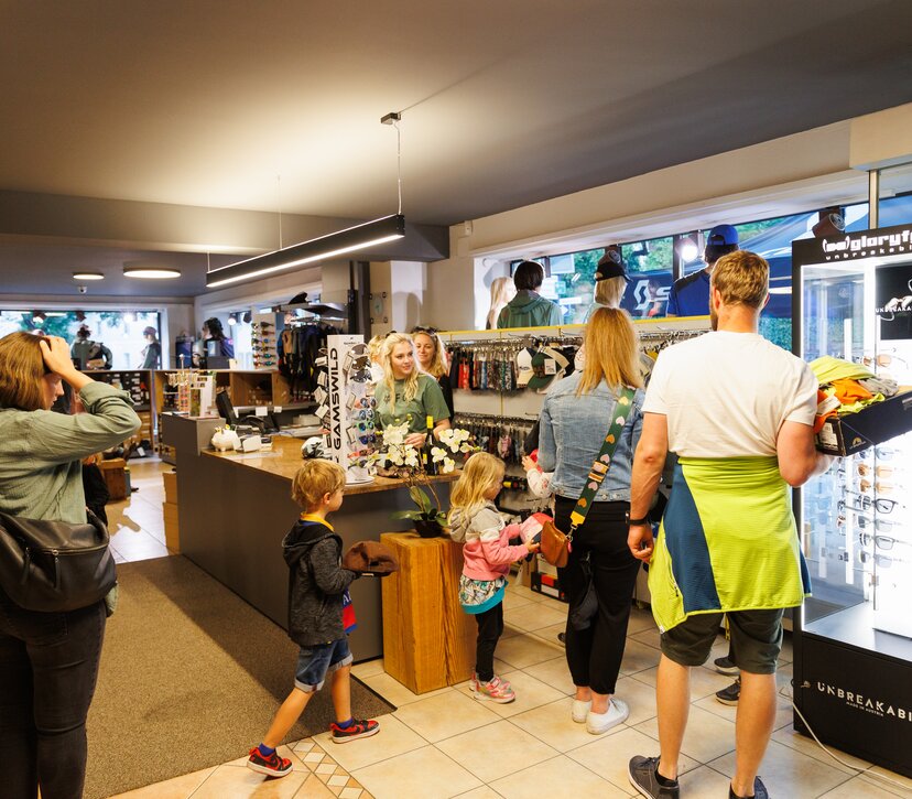 Connys Sport und Mode in Brixlegg | © WiR Alpbachtal | Maximalgrafik Personen, Männer, Frauen und Kinder, gehen durch das Geschäft von Connys Sport und Mode Brixlegg, zwei Verkäuferinnen stehen bei der Kassa. | © WiR Alpbachtal | Maximalgrafik