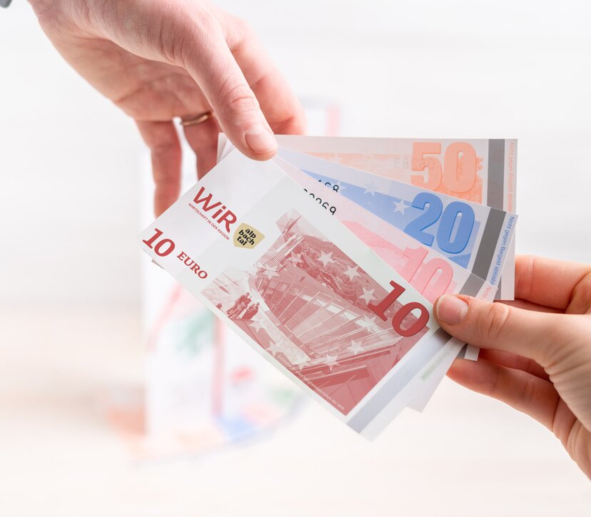 WiR-Gutscheine mit neuem Design | © WiR Alpbachtal | Genusskind Nahaufnahme von zwei Händen, die gemeinsam WiR-Gutscheine halten. | © WiR Alpbachtal | Genusskind