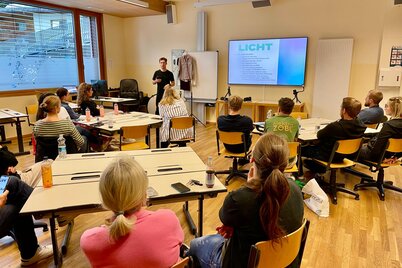 Netzwerktreffen mit Maximalgrafik | © WiR Alpbachtal Personen sitzen in einer Schulklasse und hören einem Vortragenden zu, welcher zu einer Präsentation spricht, auf der elektronischen Tafel ist eine Folie mit der großen Überschrift "Licht" zu lesen.  | © WiR Alpbachtal