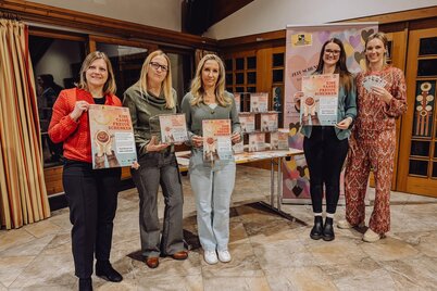 Pressefoto Eine Tasse Freude schenken | © WiR Alpbachtal 5 Frauen stehen vor einem Tisch mit Plexiglasboxen und einem Roll-up des Freiwilligen Zentrum Kitzbüheler Alpen, zwei Frauen halten ein Plakat des Projekts "Eine Tasse Freude schenken" in der Hand, eine Frau eine Plexiglasbox für die Gutscheinsammlung. | © WiR Alpbachtal